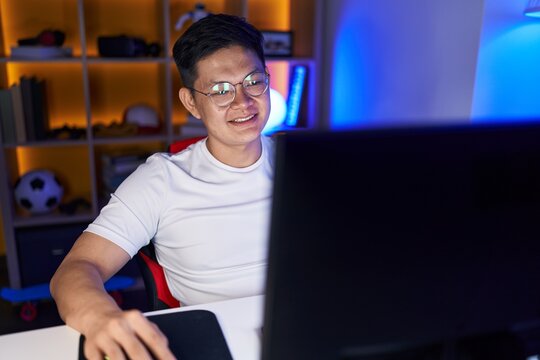 Young chinese man streamer playing video game using computer at gaming room
