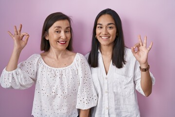 Hispanic mother and daughter together smiling positive doing ok sign with hand and fingers. successful expression.