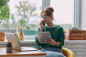 Beautiful young woman talking on mobile phone while working from home