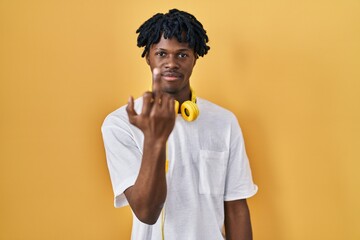 Young african man with dreadlocks standing over yellow background showing middle finger, impolite...