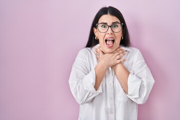 Young brunette woman standing over pink background shouting and suffocate because painful strangle. health problem. asphyxiate and suicide concept.