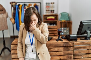 Young down syndrome woman working as manager at retail boutique tired rubbing nose and eyes feeling fatigue and headache. stress and frustration concept.