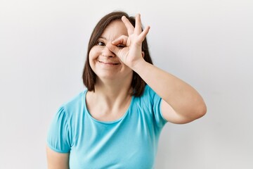 Obraz na płótnie Canvas Young down syndrome woman standing over isolated background doing ok gesture with hand smiling, eye looking through fingers with happy face.
