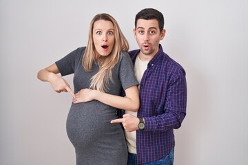 Young couple expecting a baby standing over white background pointing down with fingers showing...