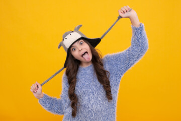 Modern teen girl wearing sweater and knitted hat on isolated yellow background. Funny face.