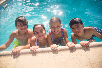 Close-up of four happy children in sparkling water of pool. Smiling girls and boys standing close...