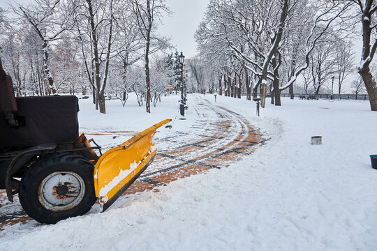 Snow Removal Tractor Cleans Alley In Park. Tractor Removing Snow, Sprinkle Salt And Sand To Prevent Slipping.