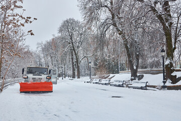 Snow removal tractor cleans alley in park. Tractor removing snow, sprinkle salt and sand to prevent...