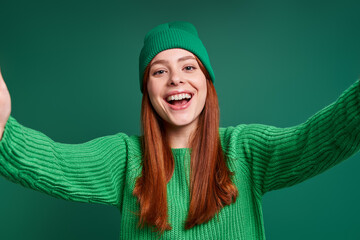 Beautiful young woman making selfie and smiling while standing against green background