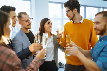 Group of young business people toasting each other and smiling while standing in the office.Partners celebrating their victory. Birthday, new year, christmas concept.
