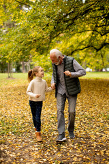 Fototapeta premium Grandfather spending time with his granddaughter in park on autumn day