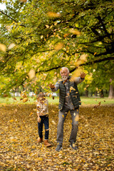 Grandfather spending time with his granddaughter in park on autumn day