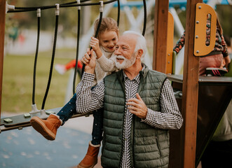 Grandfather spending time with his granddaughter in park playground on autumn day