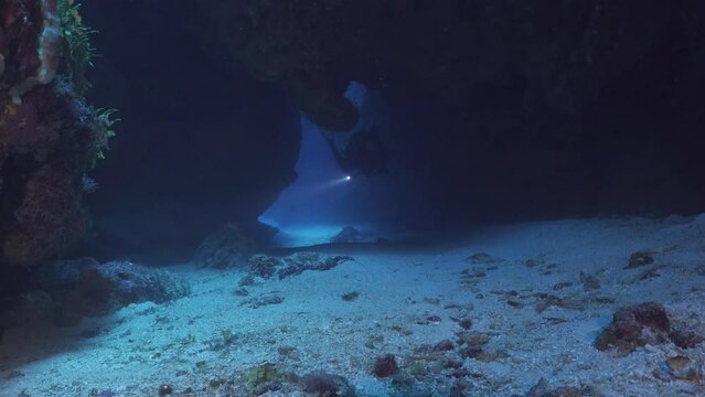 Scuba diver shows excellent buoyancy skills swimming through underwater arch.