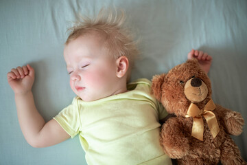 small child sleeps in bed with teddy bear. dishevelled child with blond hair lies closing eyes in bed on blue sheet.