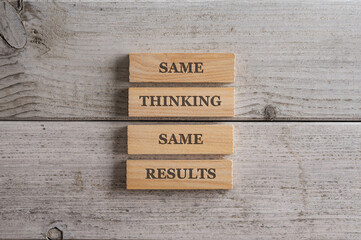 Same Thinking Same results sign written on four stacked wooden pegs