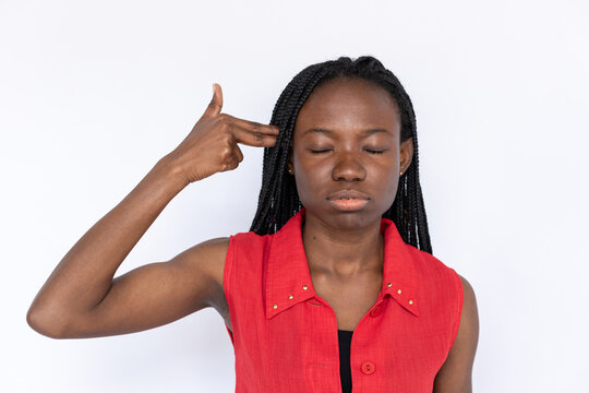 Tired woman making gun gesture. Female African American model in red vest holding two fingers at temple. Portrait, studio shot, boredom concept