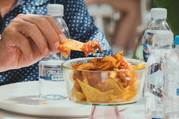 Man holding chips dipped in tortilla sauce in glass bowl. Hand of man wearing polka dot shirt.
