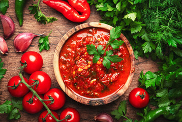 Caucasian cuisine. Traditional armenian hot adjika sauce with hot pepper, paprika, garlic and parsley on rustic wood kitchen table background, top view