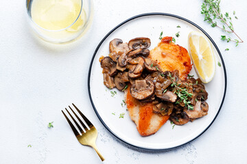 Fried chicken breast fillet with champignon mushrooms and onion in white wine sauce with thyme on plate, white table background, top view