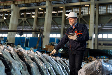 A machine factory engineer is inspecting the machines in the factory with a tablet or laptop and with a deliberate eye check. The factory is big and old.