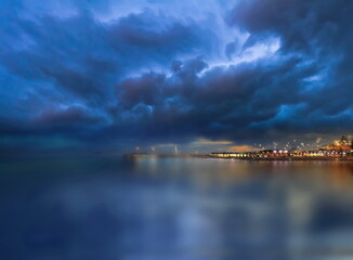 Night city blurred light on horizon at sea blue water wave and Aurora borealis on starry sky