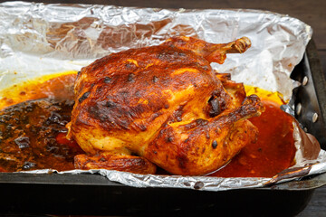 Whole baked chicken carcass with a crust on a foil on a baking sheet.