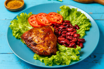 Chicken with red beans garnished with tomato on lettuce leaves in a blue plate on a blue wooden table.
