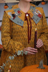 Fototapeta premium Fashion woman, girl in dress with patchwork collar. Embroidered collar. Halloween style, look, outfit. Decor with candles and pumpkins. Halloween decoration at home, indoor. Autumn Halloween decor