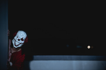 Asian handsome man wear clown mask with weapon at the night scene,Halloween festival concept,Horror scary photo of a killer in orange cloth,Evil clown charactor