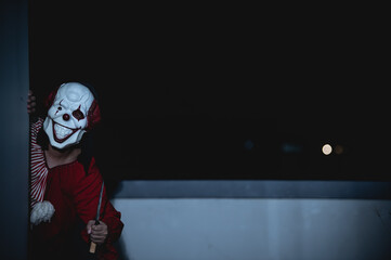 Obraz na płótnie Canvas Asian handsome man wear clown mask with weapon at the night scene,Halloween festival concept,Horror scary photo of a killer in orange cloth,Evil clown charactor