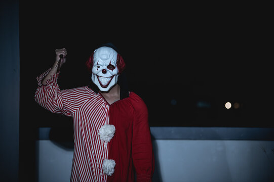 Asian handsome man wear clown mask with weapon at the night scene,Halloween festival concept,Horror scary photo of a killer in orange cloth,Evil clown charactor