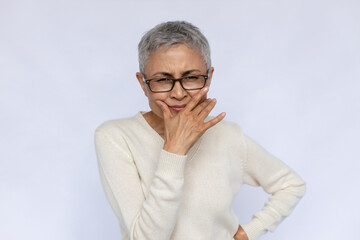 Portrait of senior woman looking at camera in doubt. Mature Caucasian woman with bad sight wearing eyeglasses and white jumper squinting eyes over white background. Doubt and uncertainty concept