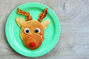 Reindeer pancake made it from pancakes,bacon,cheeses,black olives and raspberry on green plate with...