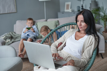 woman using laptop with interest at home while child relax on sofa