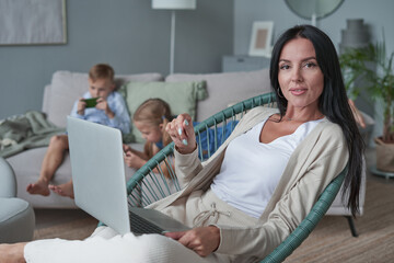 woman using laptop with interest at home while child relax on sofa