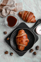 Delicious crispy croissant with chocolate with a cup of invigorating coffee on a light concrete background