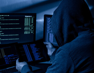 Hooded hacker attempting data breach at night in a dark private office