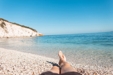 Fototapeta na wymiar Man lies and rest on the beach by the clear azure sea with a rock on the island of Elba, Italy