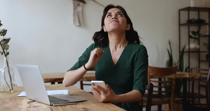Stressed woman reading bad news in SMS sits at desk with smartphone feels disappointed, looks concerned and angry. Device malfunction, lost information, missed important call, Wi-Fi connection loss
