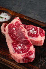 Two juicy raw beef steaks on a board with salt for grilling