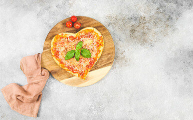 Hot pizza heart on a round wooden cutting board with cherry tomatoes on a gray cement table .