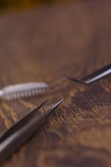 Sharp tweezers and eyelash extension brush on wooden background