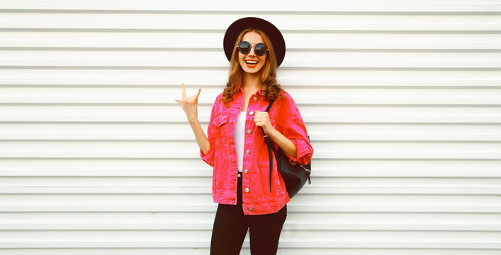Portrait of stylish modern smiling young woman wearing pink jacket, black round hat and backpack on white background, blank copy space for advertising text