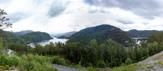 Naklejka na ściany i meble Panoramic view of Norwegian fjord seawater inlet between green mountains with tall vegetation and infrastructure of roads and bridges. 