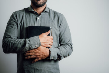 Standing man holding and hugging the bible on his chest.