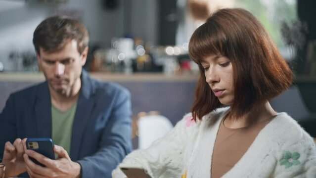 A man and a woman on a date in a cafe are sitting on the phones. The girl looks at the guy with a negative emotion. Life online with a smartphone. High quality 4k footage