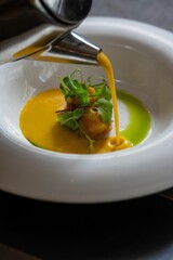 Vertical closeup of a pumpkin soup pouring into a white ceramic bowl