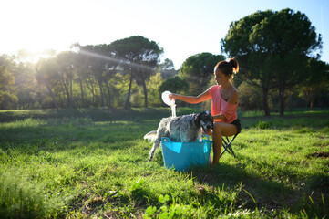 Middle-aged woman bathing her dog in the garden on a sunny day.