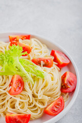 Spaghetti with fresh cherry tomatoes on a white plate. Boiled spaghetti pasta with vegetables on a gray background. Close-up